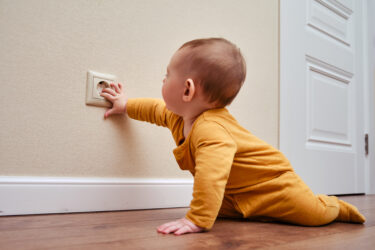 Baby toddler reaches into the electrical outlet on the home wall with his hand. Danger and protection of child fingers from electric shock, aged 6-11 months